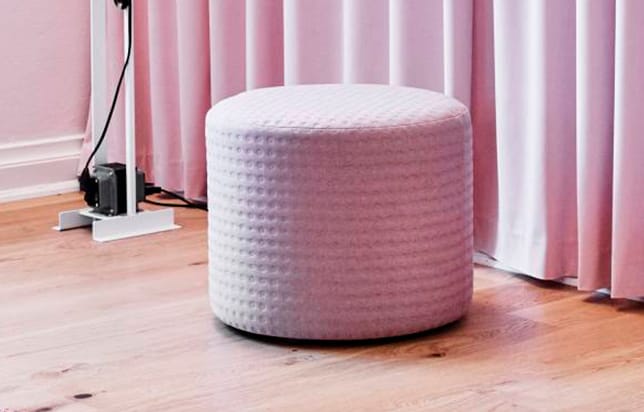 A pink cylindrical stool in front of a pink curtain.