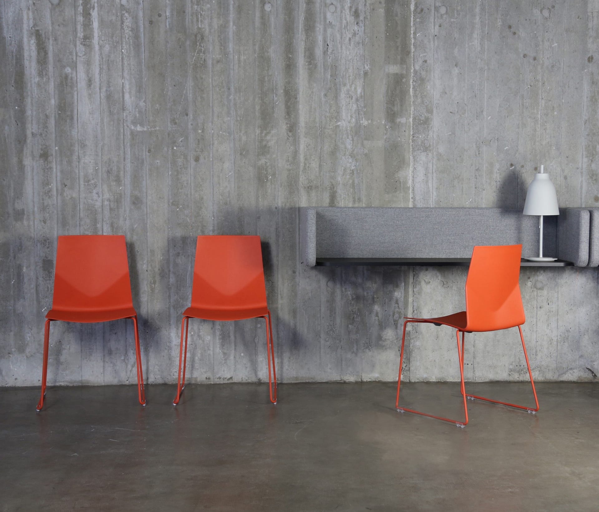 Three orange chairs in front of a concrete wall.