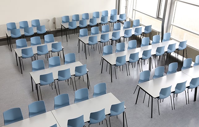 A classroom with rows of blue meeting table chairs and windows.