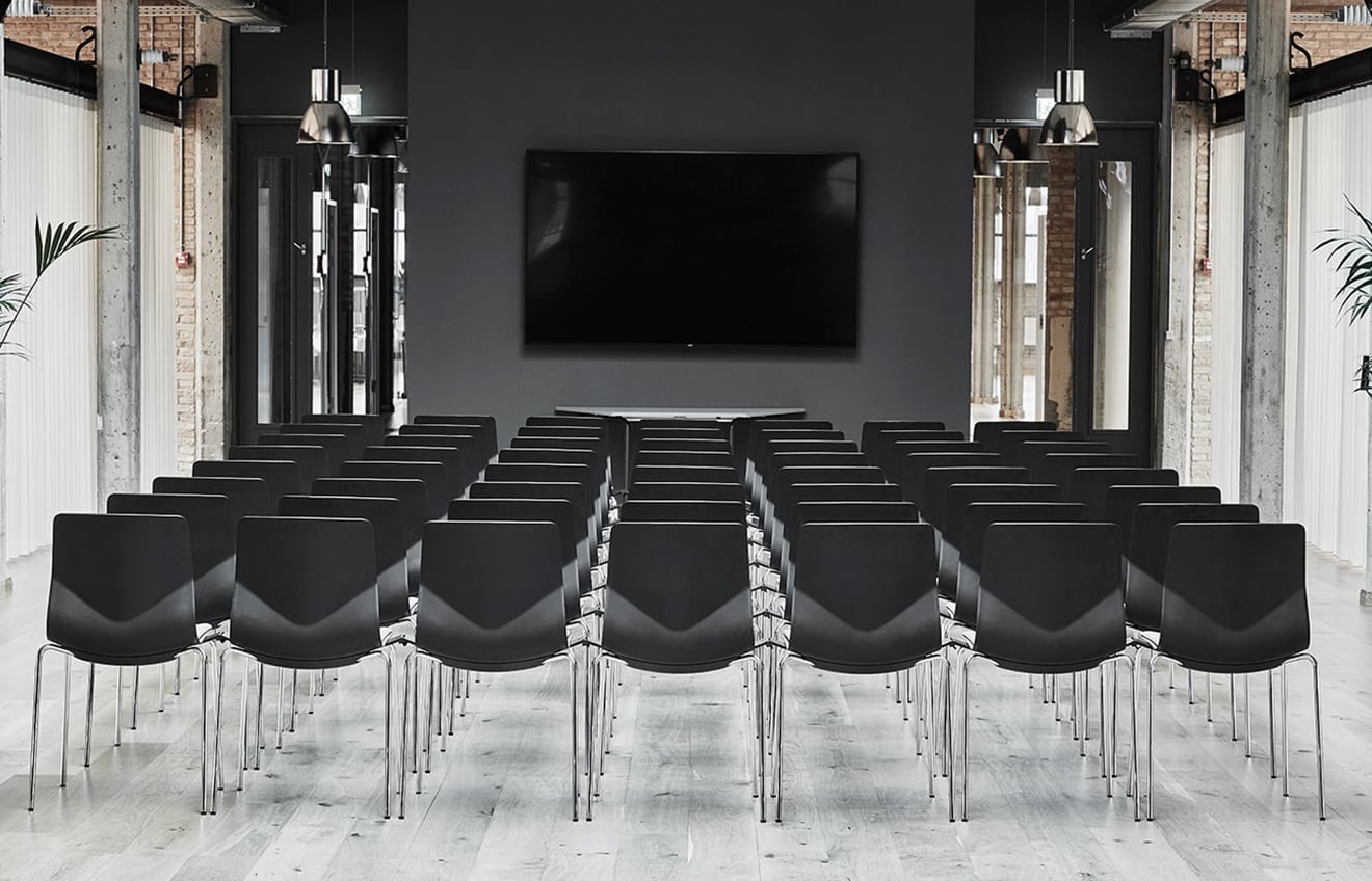 A room with rows of black meeting room chairs and a tv.