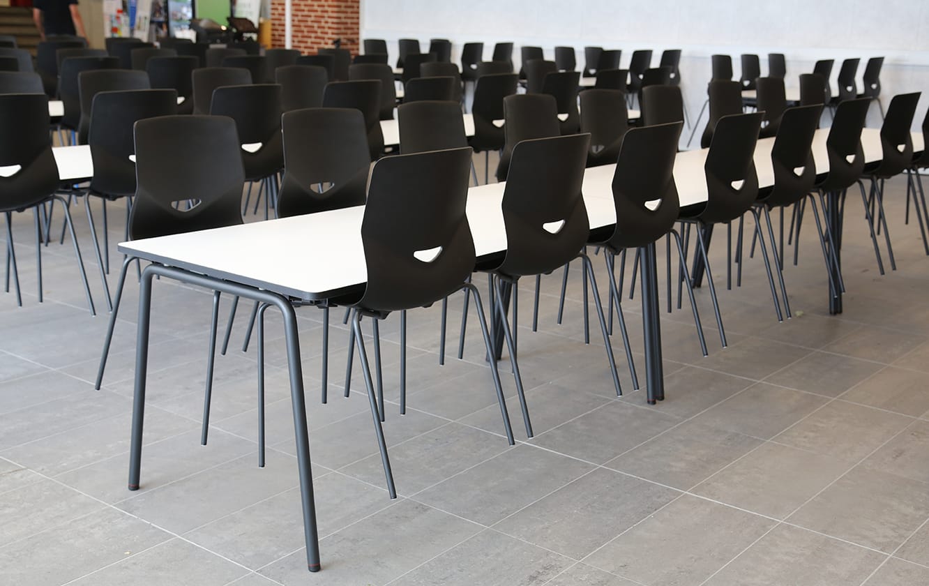 A long row of black meeting table chairs in a classroom.