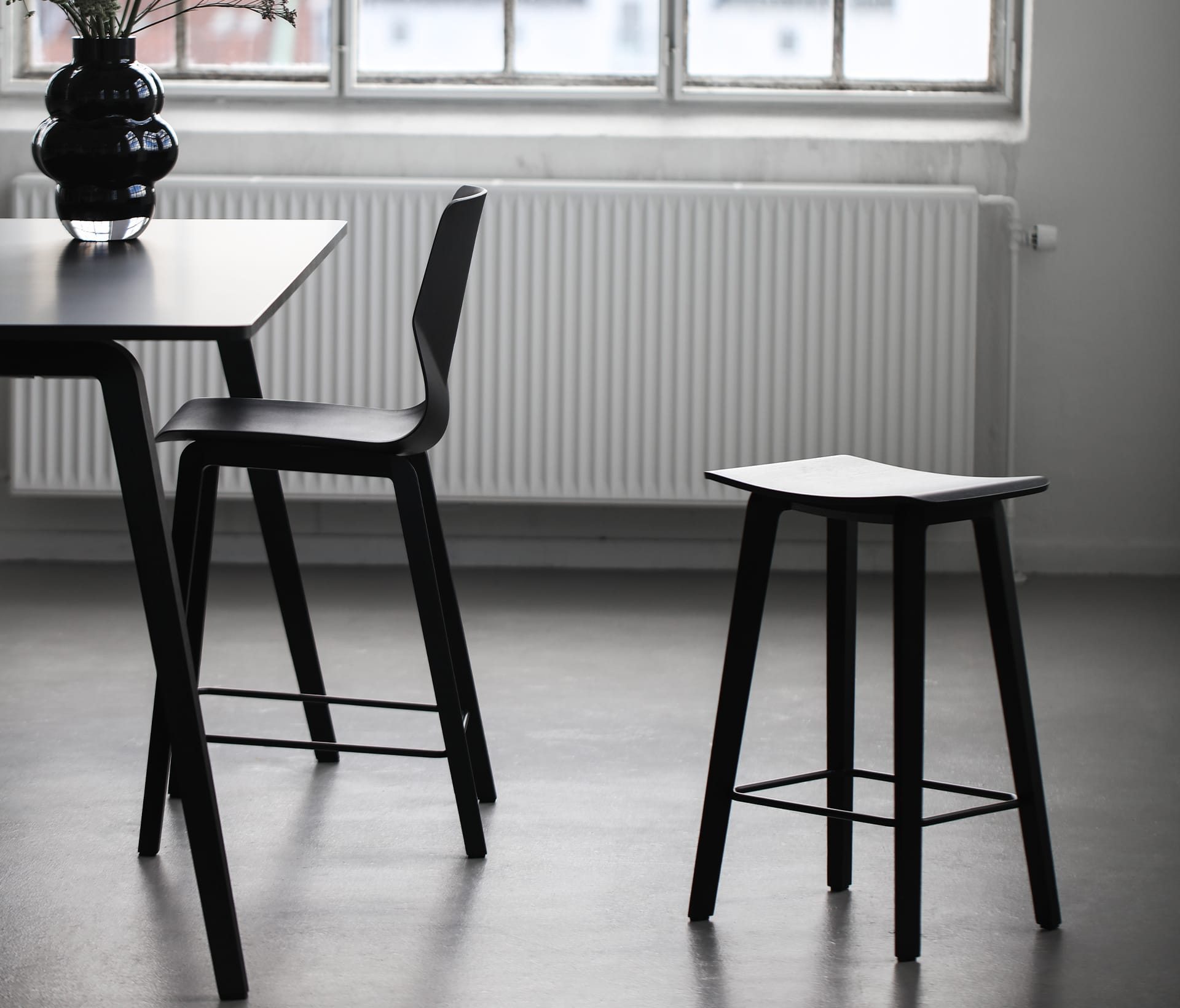 A dining table with two black stools in front of a window.