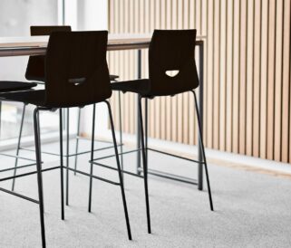 Four black stools in an office with a wooden table.