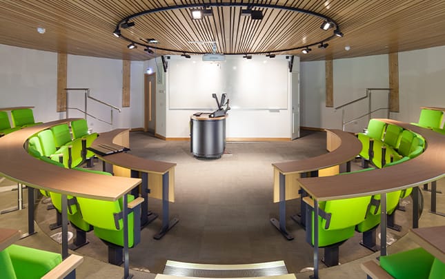 A lecture room with green chairs and a round table.