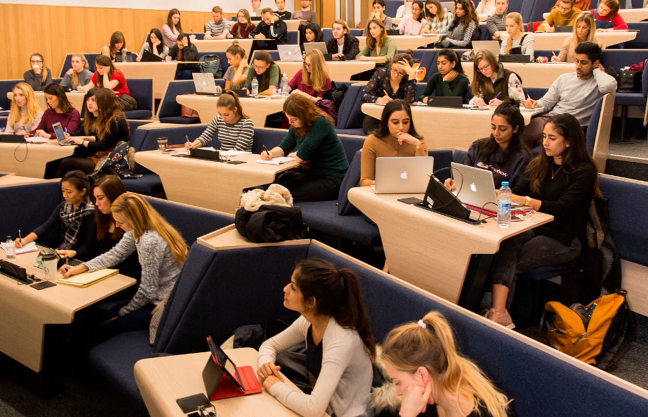 A lecture hall with many people sitting at desks on lecture hall seating