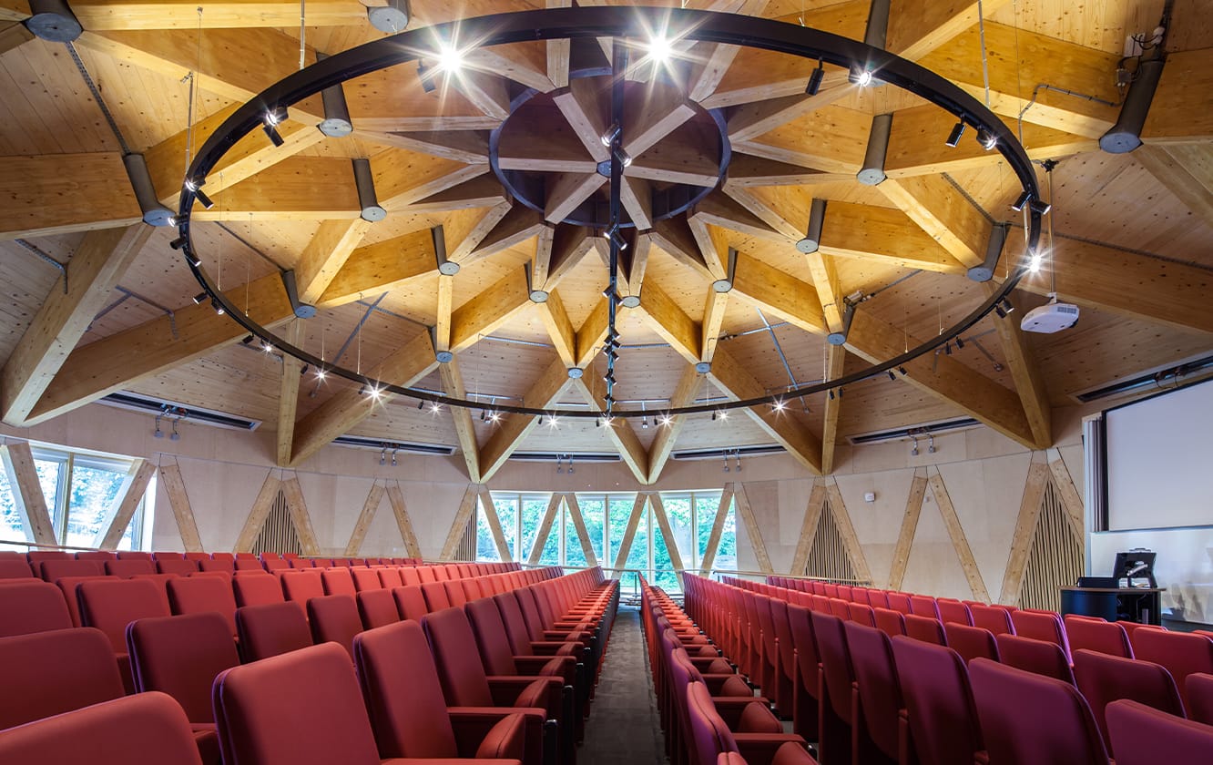 An auditorium with rows of red auditorium seating and a wooden ceiling.