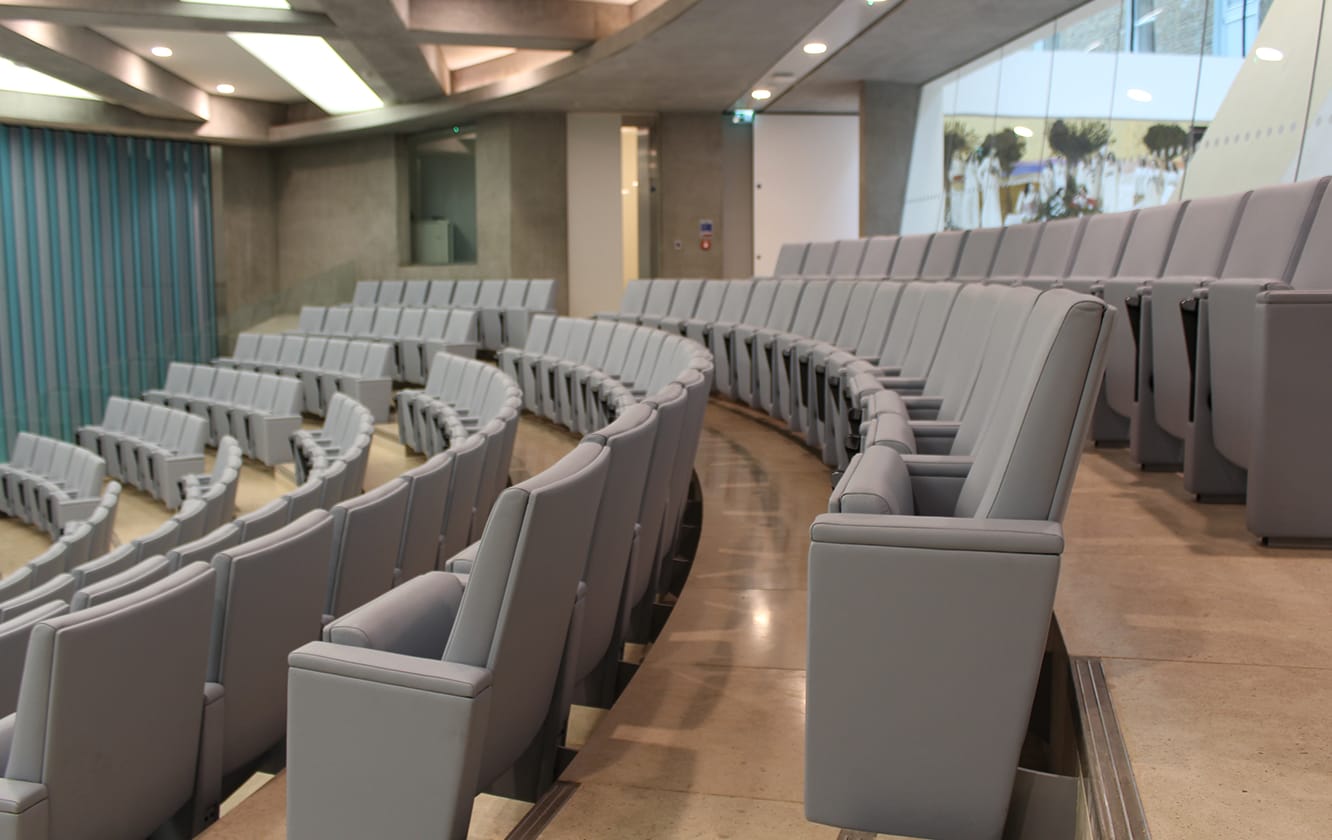 A row of grey auditorium seating in a large auditorium.