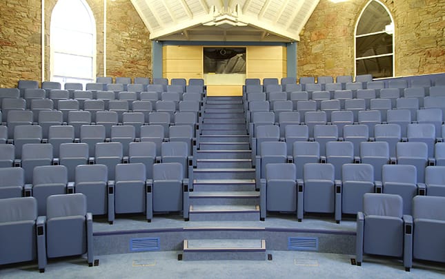 A blue carpeted auditorium with rows of tip up seating