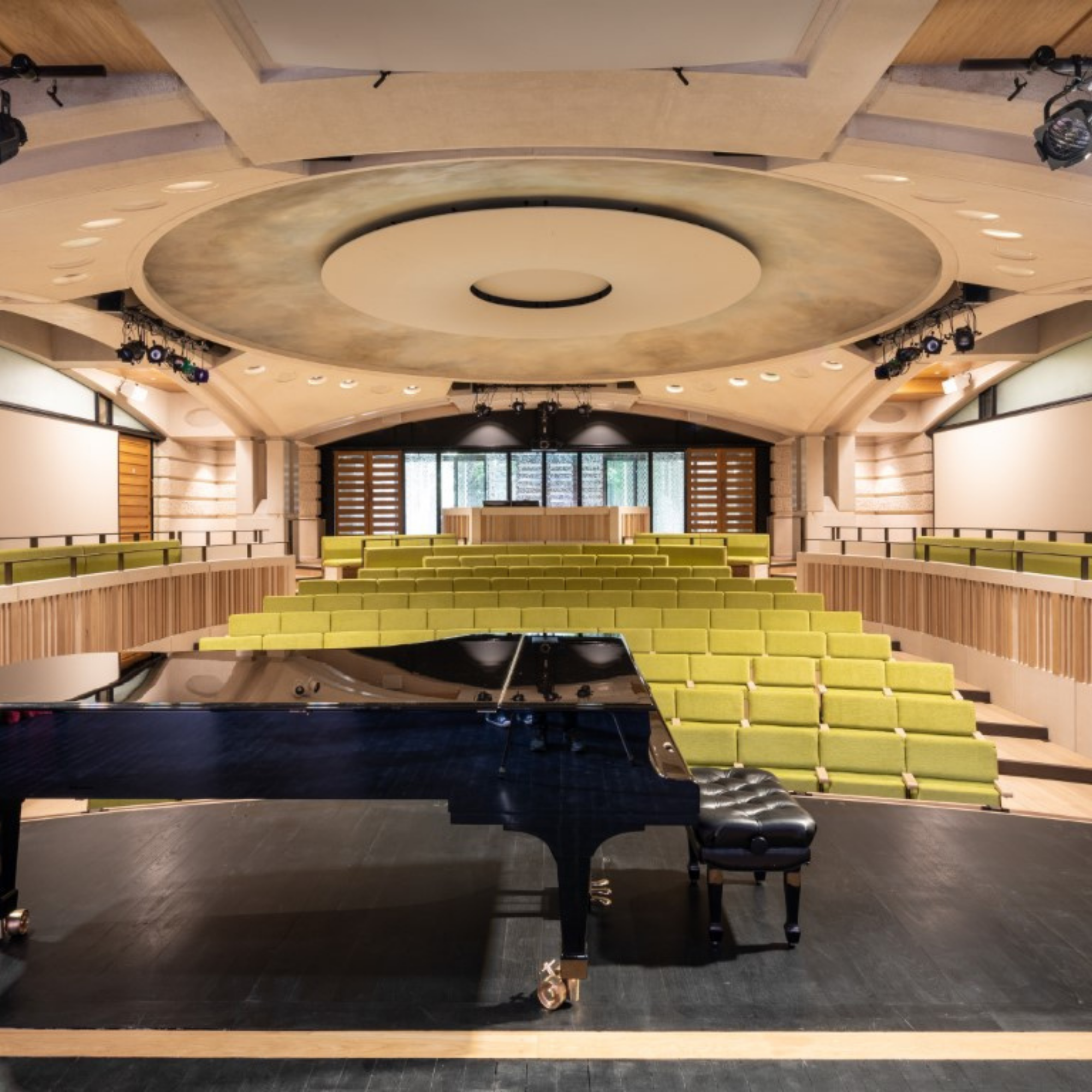 An auditorium with a piano and green auditorium seating
