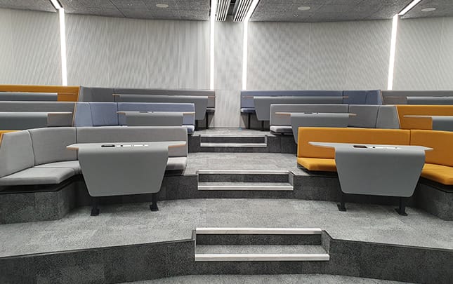 A lecture hall with blue and orange lecture hall seating and desks