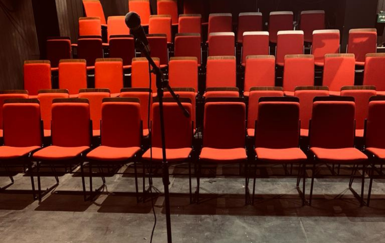 An empty auditorium with red chairs and a microphone.