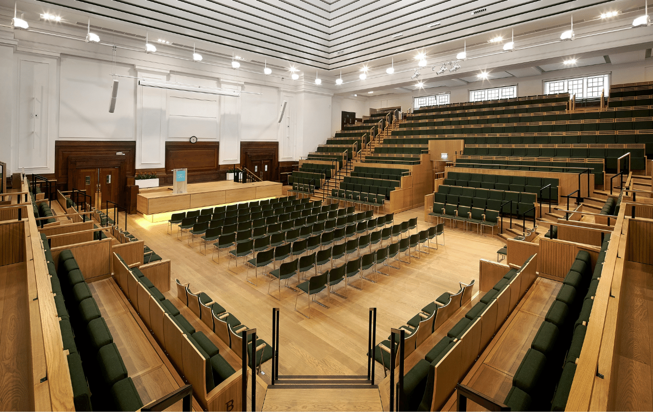 A large auditorium with green auditorium seating and a wooden floor.