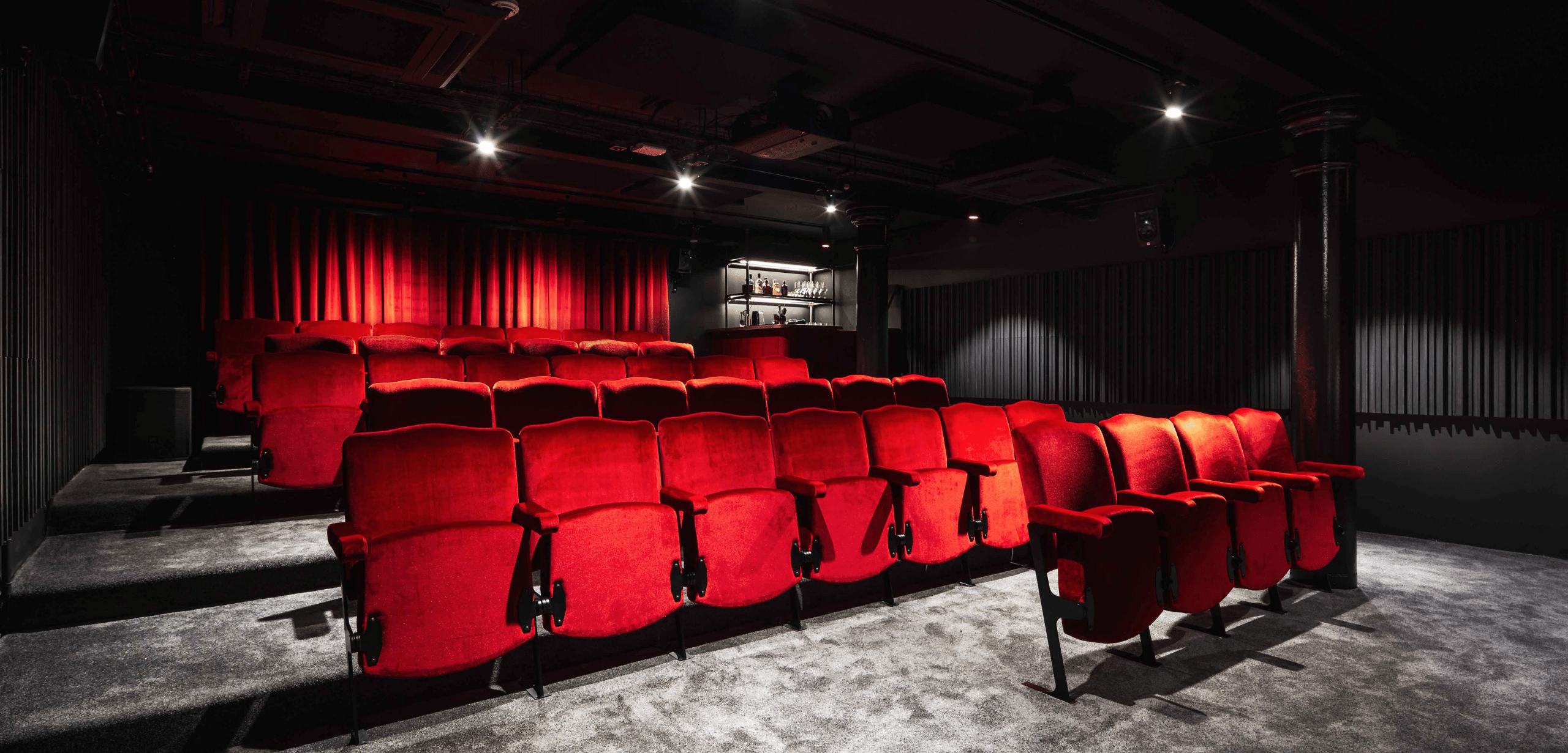 A movie theater with red theater style seating and a black curtain.