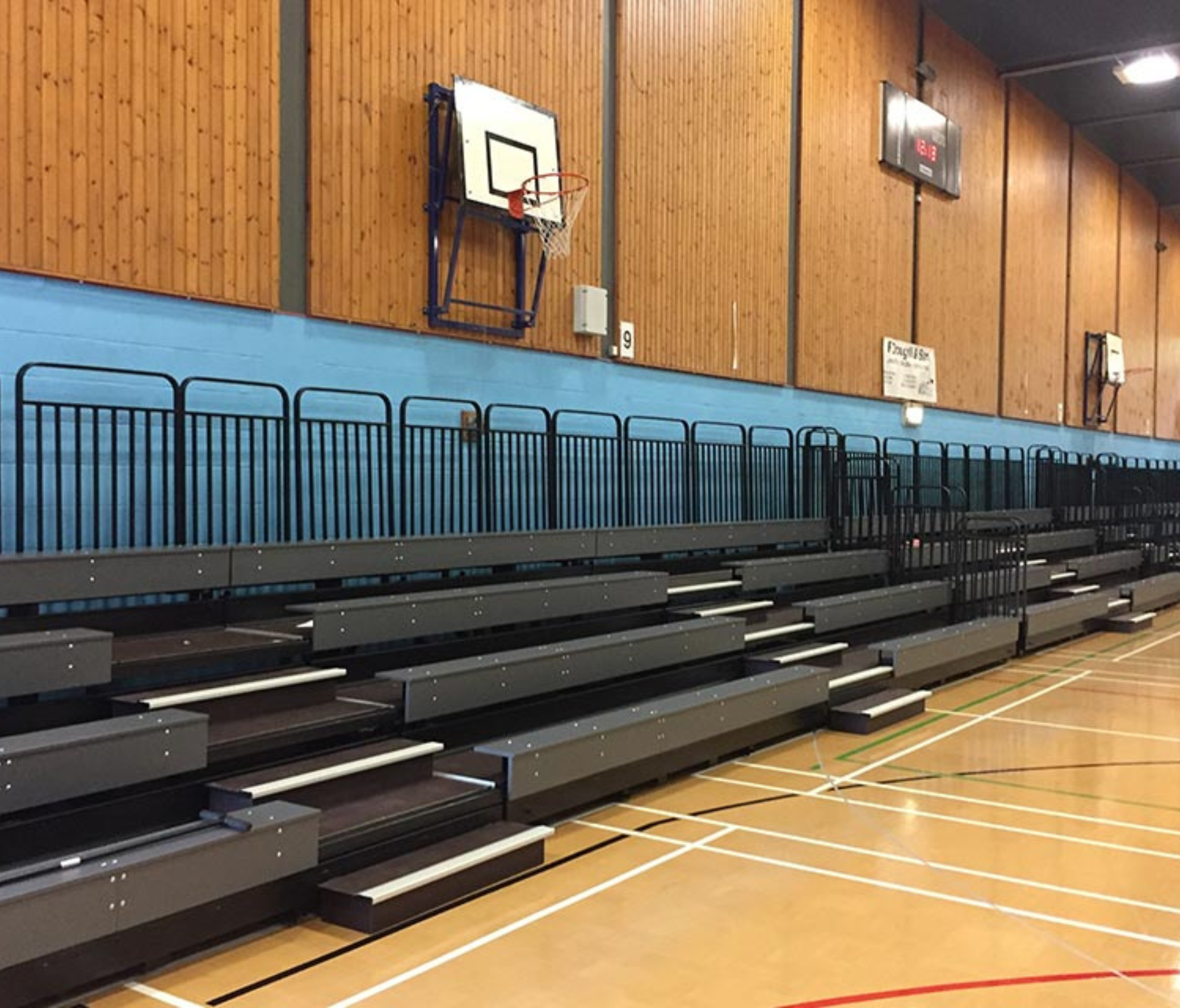 A gym with rows of bleachers and a basketball hoop.