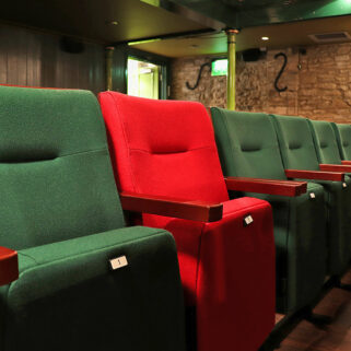 A row of red and green tip up seating in an auditorium.