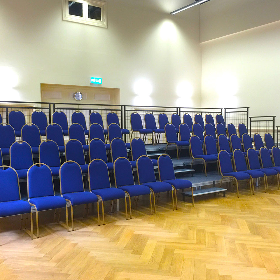 A large auditorium with rows of blue chairs on staging.