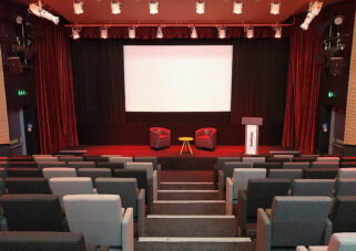An auditorium with rows of tip up seating and a projection screen.