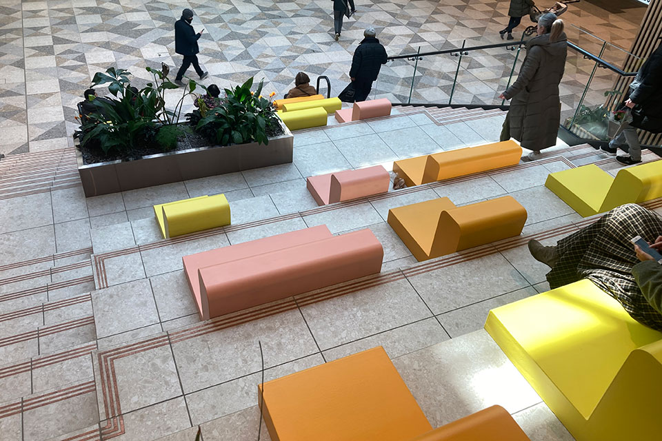 A group of people sitting on colourful tiered seating solutions in a lobby.