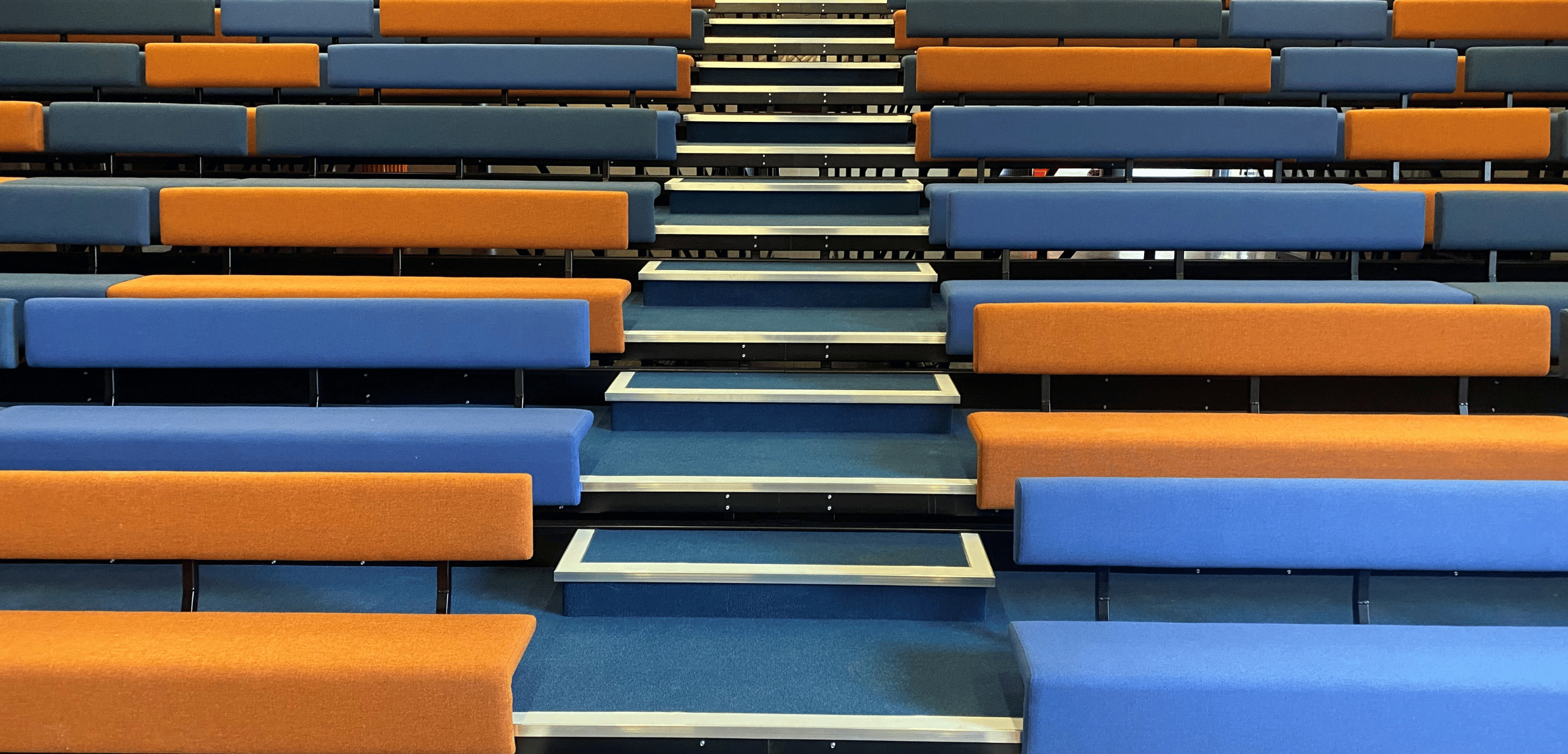 A row of blue and orange auditorium seating in an auditorium.