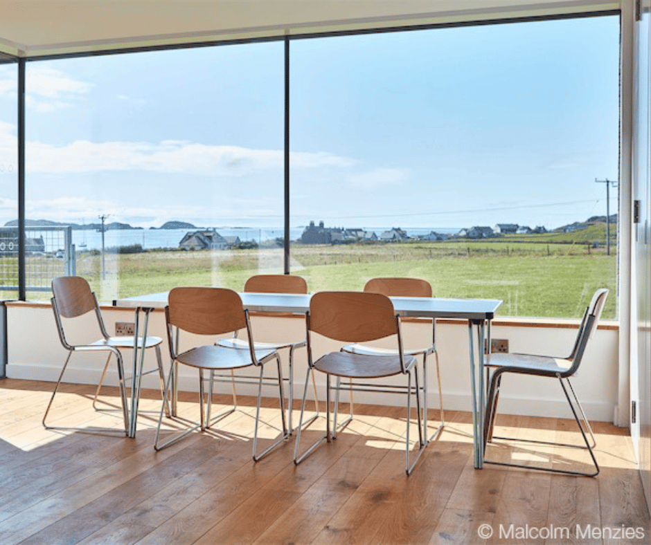 A dining table and chairs infront of large windows overlooking a field.