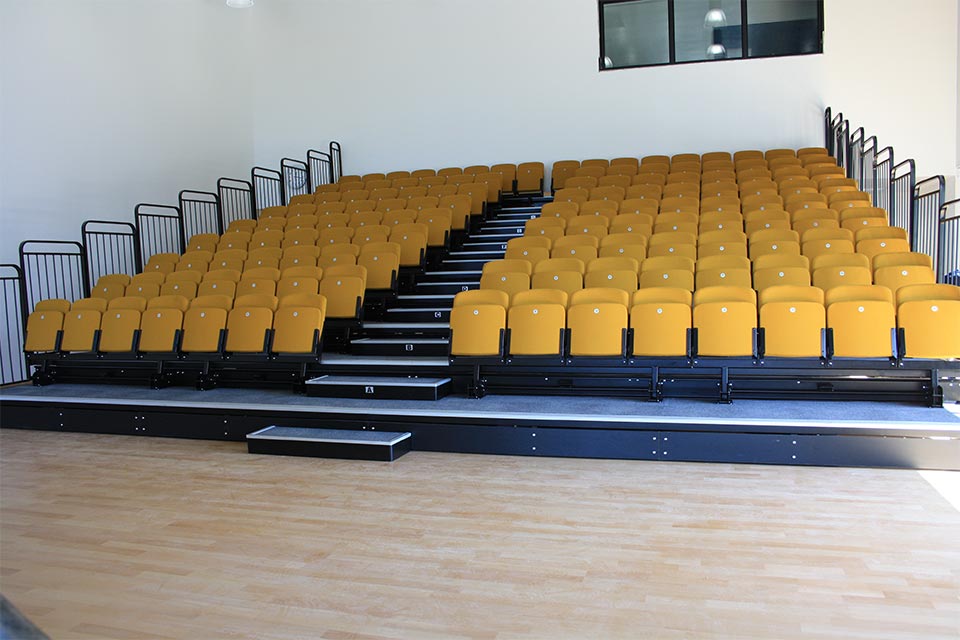 A large auditorium with yellow tiered seating and stairs.