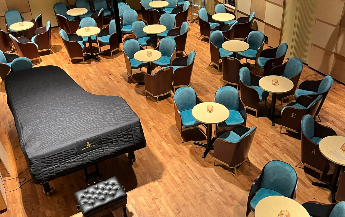 A room with hospitality seating, tables and chairs and a piano.